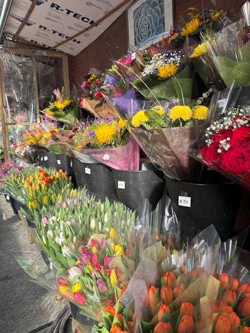 An indoor display of freshly arranged flower bouquets at a floral shop, featuring vibrant tulips in shades of pink, orange, yellow, and white, wrapped in clear and colored cellophane. Behind the tulip